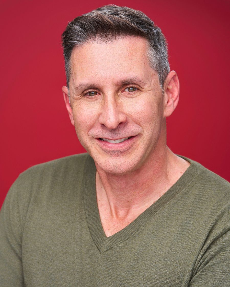 Sean Kramer smiling in an olive sweater against a red background